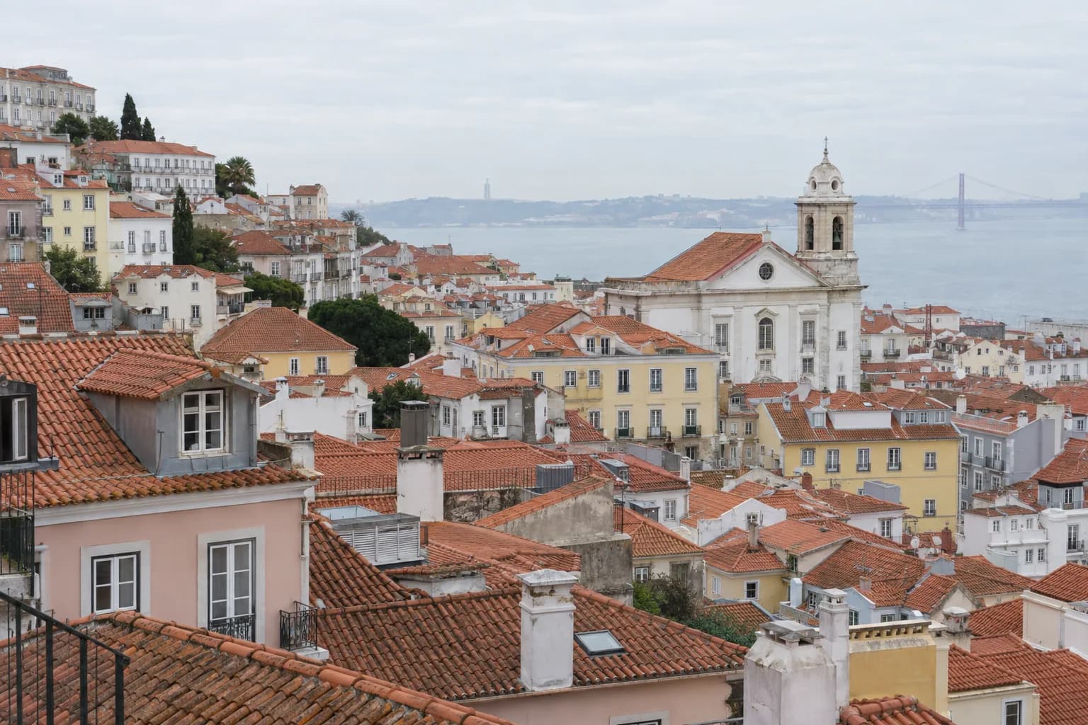 Telhados de telha cerâmica de um bairro numa encosta, com chaminés e a torre de uma igreja