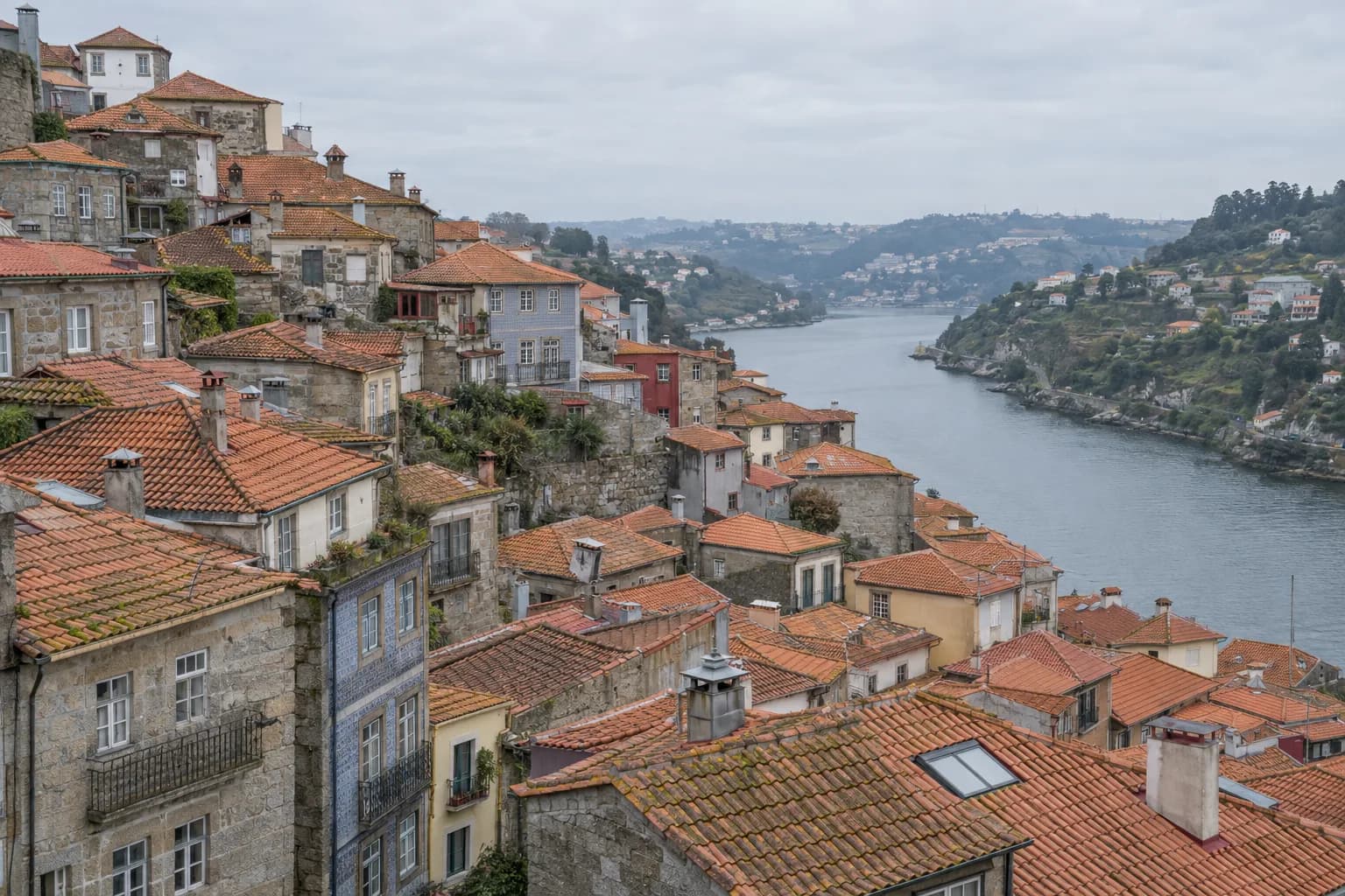 Casas antigas de granito e telhados de telha numa encosta, com chaminés e um vale ao fundo